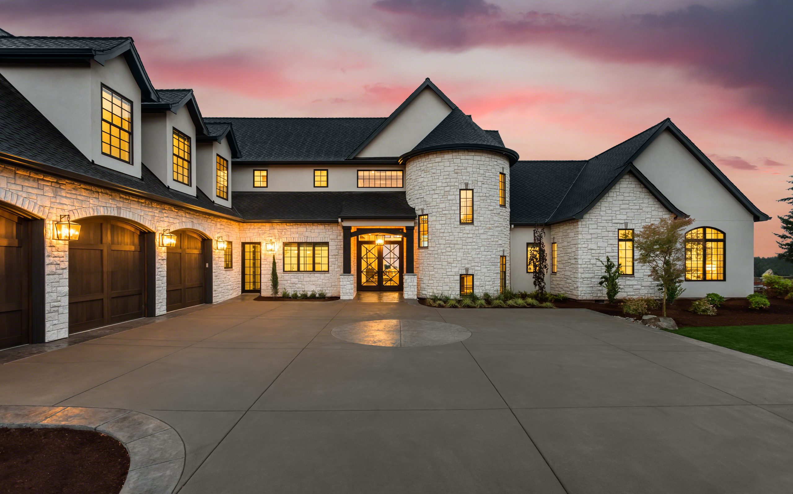 Stunning Luxury Home Exterior at Sunset with Colorful Sky and Expansive Driveway. This Mansion has Three Garages, Turret Style Tower, and Two Floors